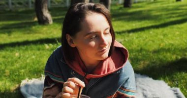 Güzel genç bir kadın parkta kokteyl içer, bahar güneşinin tadını çıkarır. Bahar limonatası. - Evet. Yüksek kalite 4k görüntü