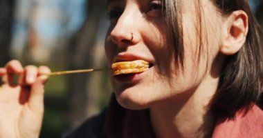 Güzel genç bir kadın parkta sokak yemeği yiyor, bahar güneşinin tadını çıkarıyor. Kız ızgara karides yiyor. Yüksek kalite 4k görüntü