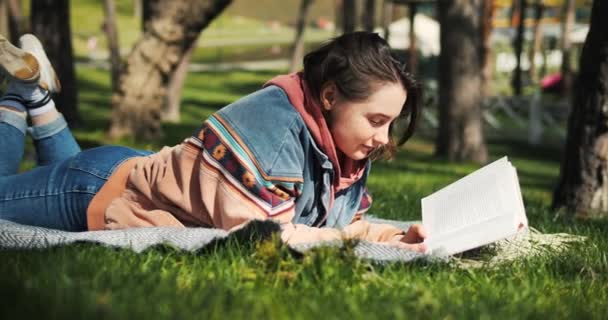 若い大人の女性は公園で本を読んでいる 春の日差しで外で読書する 女の子は本を楽しんでいる 高品質の4K映像 — ストック動画