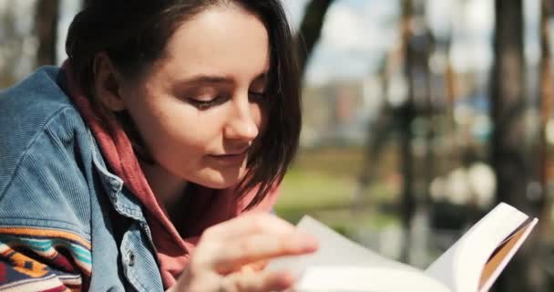 若い大人の女性は公園で本を読んでいる 春の日差しで外で読書する 女の子は本を楽しんでいる 高品質の4K映像 — ストック動画
