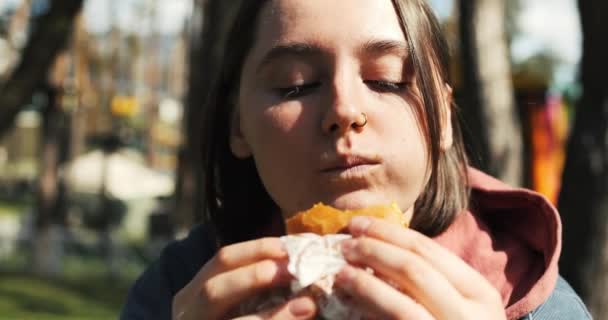아름다운 소녀는 공원에서 음식을 먹는다 여자는 햇빛에 햄버거를 즐긴다 고품질 — 비디오
