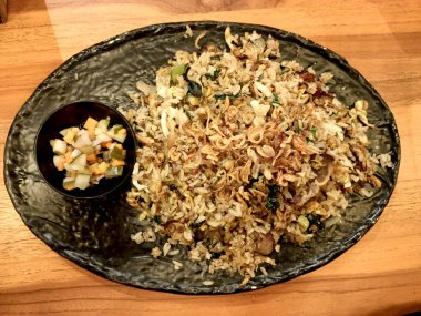 Endonezya 'nın tipik yiyeceklerinden biri olan Nasi Goreng. ... turşu ve kızarmış soğan parçacıklarıyla dolu siyah bir tabakta servis edilir..