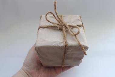  El işi ambalajında bir paket, turnikeyle bağlanmış, beyaz bir arka planda el ele tutulmuş.