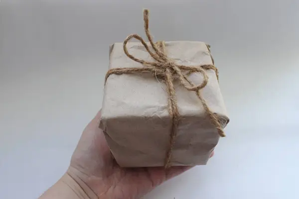  El işi ambalajında bir paket, turnikeyle bağlanmış, beyaz bir arka planda el ele tutulmuş.