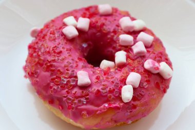 Şekerlemeli pembe çörek ve beyaz bir tabakta renkli şekerlemeler, hafif bir arkaplanda tatlıya yakın plan.