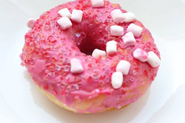Şekerlemeli pembe çörek ve beyaz bir tabakta renkli şekerlemeler, hafif bir arkaplanda tatlıya yakın plan.