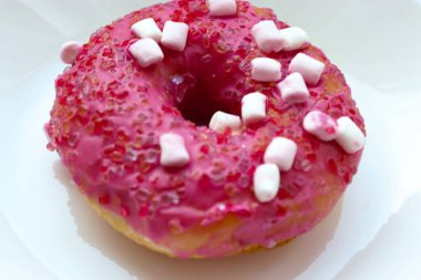 Şekerlemeli pembe çörek ve beyaz bir tabakta renkli şekerlemeler, hafif bir arkaplanda tatlıya yakın plan.