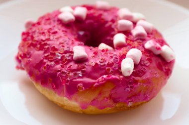 Şekerlemeli pembe çörek ve beyaz bir tabakta renkli şekerlemeler, hafif bir arkaplanda tatlıya yakın plan.