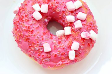 Şekerlemeli pembe çörek ve beyaz bir tabakta renkli şekerlemeler, hafif bir arkaplanda tatlıya yakın plan.
