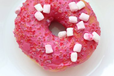 Şekerlemeli pembe çörek ve beyaz bir tabakta renkli şekerlemeler, hafif bir arkaplanda tatlıya yakın plan.