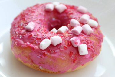 Şekerlemeli pembe çörek ve beyaz bir tabakta renkli şekerlemeler, hafif bir arkaplanda tatlıya yakın plan.