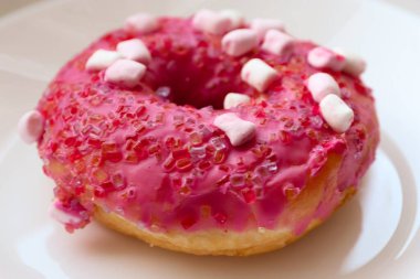 Şekerlemeli pembe çörek ve beyaz bir tabakta renkli şekerlemeler, hafif bir arkaplanda tatlıya yakın plan.