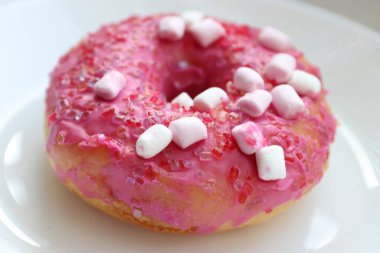 Şekerlemeli pembe çörek ve beyaz bir tabakta renkli şekerlemeler, hafif bir arkaplanda tatlıya yakın plan.