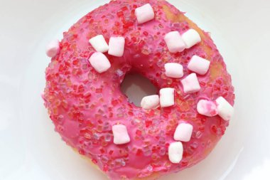 Şekerlemeli pembe çörek ve beyaz bir tabakta renkli şekerlemeler, hafif bir arkaplanda tatlıya yakın plan.