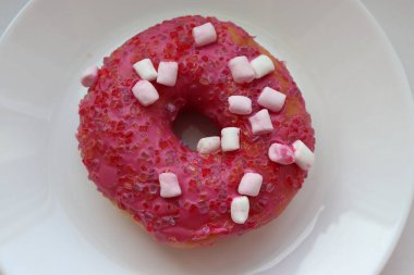 Şekerlemeli pembe çörek ve beyaz bir tabakta renkli şekerlemeler, hafif bir arkaplanda tatlıya yakın plan.
