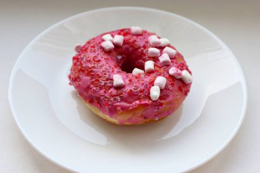 Şekerlemeli pembe çörek ve beyaz bir tabakta renkli şekerlemeler, hafif bir arkaplanda tatlıya yakın plan.