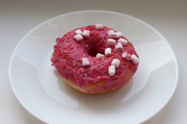 Şekerlemeli pembe çörek ve beyaz bir tabakta renkli şekerlemeler, hafif bir arkaplanda tatlıya yakın plan.