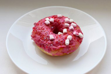 Şekerlemeli pembe çörek ve beyaz bir tabakta renkli şekerlemeler, hafif bir arkaplanda tatlıya yakın plan.