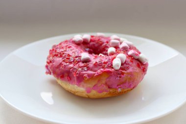 Şekerlemeli pembe çörek ve beyaz bir tabakta renkli şekerlemeler, hafif bir arkaplanda tatlıya yakın plan.