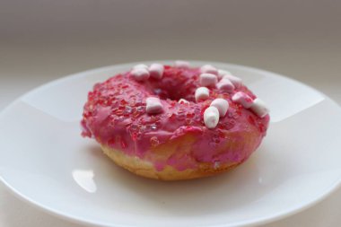 Şekerlemeli pembe çörek ve beyaz bir tabakta renkli şekerlemeler, hafif bir arkaplanda tatlıya yakın plan.