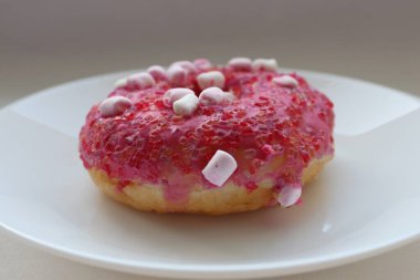 Şekerlemeli pembe çörek ve beyaz bir tabakta renkli şekerlemeler, hafif bir arkaplanda tatlıya yakın plan.