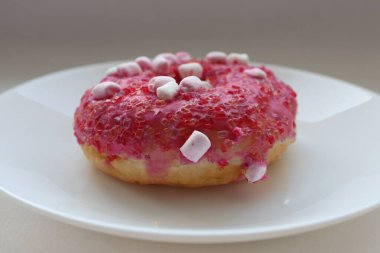 Şekerlemeli pembe çörek ve beyaz bir tabakta renkli şekerlemeler, hafif bir arkaplanda tatlıya yakın plan.