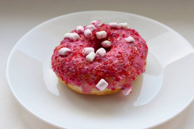 Şekerlemeli pembe çörek ve beyaz bir tabakta renkli şekerlemeler, hafif bir arkaplanda tatlıya yakın plan.