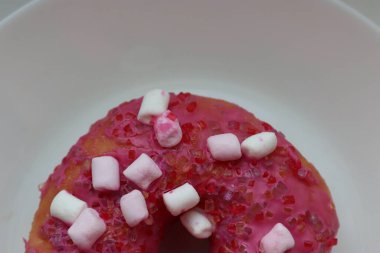 Şekerlemeli pembe çörek ve beyaz bir tabakta renkli şekerlemeler, hafif bir arkaplanda tatlıya yakın plan.