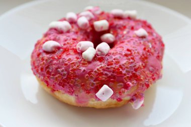 Şekerlemeli pembe çörek ve beyaz bir tabakta renkli şekerlemeler, hafif bir arkaplanda tatlıya yakın plan.