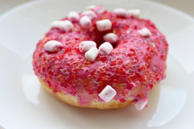 Şekerlemeli pembe çörek ve beyaz bir tabakta renkli şekerlemeler, hafif bir arkaplanda tatlıya yakın plan.