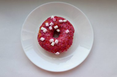 Şekerlemeli pembe çörek ve beyaz bir tabakta renkli şekerlemeler, hafif bir arkaplanda tatlıya yakın plan.