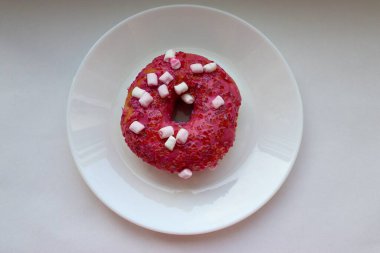 Şekerlemeli pembe çörek ve beyaz bir tabakta renkli şekerlemeler, hafif bir arkaplanda tatlıya yakın plan.