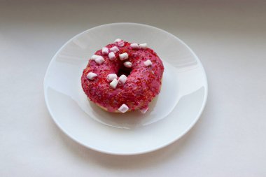 Şekerlemeli pembe çörek ve beyaz bir tabakta renkli şekerlemeler, hafif bir arkaplanda tatlıya yakın plan.