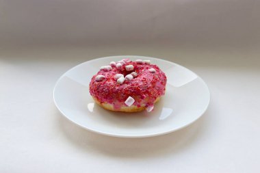 Şekerlemeli pembe çörek ve beyaz bir tabakta renkli şekerlemeler, hafif bir arkaplanda tatlıya yakın plan.