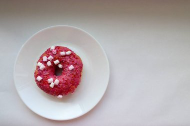 Şekerlemeli pembe çörek ve beyaz bir tabakta renkli şekerlemeler, hafif bir arkaplanda tatlıya yakın plan.