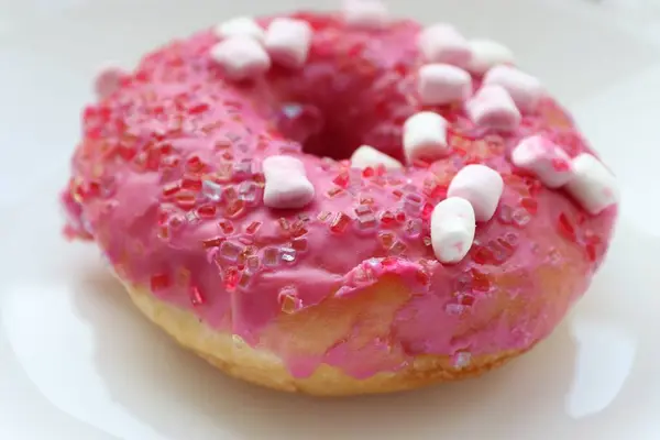 Şekerlemeli pembe çörek ve beyaz bir tabakta renkli şekerlemeler, hafif bir arkaplanda tatlıya yakın plan.