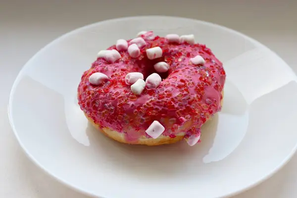 Şekerlemeli pembe çörek ve beyaz bir tabakta renkli şekerlemeler, hafif bir arkaplanda tatlıya yakın plan.
