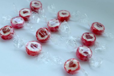 Beyaz arka plan konseptine dağılmış kırmızı kalpler ve renkli şekerler. Sevgililer Günü için şenlikli tatlılar, romantizm ve neşeli ruh hali.