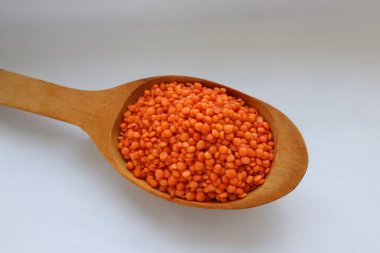 Beyaz arka plan konsepti üzerine tahta kaşıkta kırmızı mercimek. Sağlıklı gıda, bitkisel protein ve doğal mutfak malzemeleri estetiği.