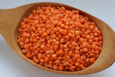 Beyaz arka plan konsepti üzerine tahta kaşıkta kırmızı mercimek. Sağlıklı gıda, bitkisel protein ve doğal mutfak malzemeleri estetiği.