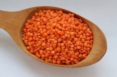 Beyaz arka plan konsepti üzerine tahta kaşıkta kırmızı mercimek. Sağlıklı gıda, bitkisel protein ve doğal mutfak malzemeleri estetiği.