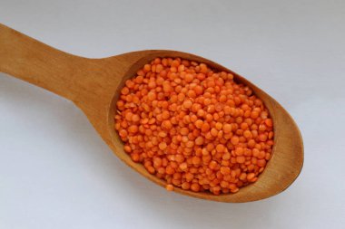 Beyaz arka plan konsepti üzerine tahta kaşıkta kırmızı mercimek. Sağlıklı gıda, bitkisel protein ve doğal mutfak malzemeleri estetiği.