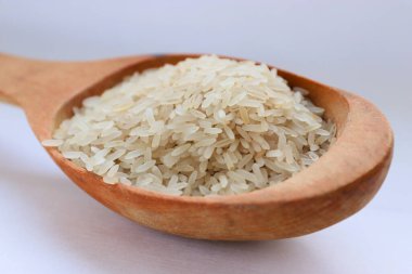 Beyaz arka planda ahşap bir kaşıkta beyaz pirinç, yakın plan doğal beslenme kavramı, görsel saflık ve sağlıklı yaşam tarzı için mutfak sadeliği.