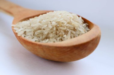 Beyaz arka planda ahşap bir kaşıkta beyaz pirinç, yakın plan doğal beslenme kavramı, görsel saflık ve sağlıklı yaşam tarzı için mutfak sadeliği.