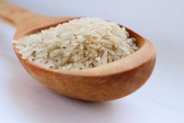 Beyaz arka planda ahşap bir kaşıkta beyaz pirinç, yakın plan doğal beslenme kavramı, görsel saflık ve sağlıklı yaşam tarzı için mutfak sadeliği.