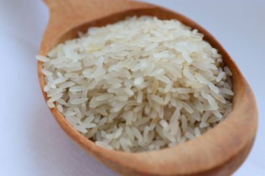 Beyaz arka planda ahşap bir kaşıkta beyaz pirinç, yakın plan doğal beslenme kavramı, görsel saflık ve sağlıklı yaşam tarzı için mutfak sadeliği.