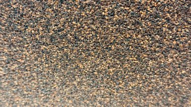 Kum benzeri parçacıklar içeren tanecikli bir yüzeye yakın çekim. Kahverengi, bronzlaşmış ve siyah granüller içeren doğal doku..