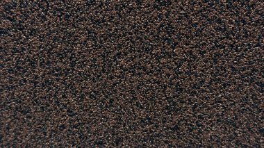 Koyu tanecikli bir yüzeye yakın çekim, yoğun bir şekilde paketlenmiş küçük kahverengi ve siyah tanecikler, teknik bir karakterle tek bir doku oluşturur..