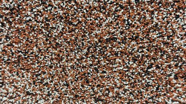 Çok renkli çakıl taşlarıyla kaplı, kahverengi, beyaz ve siyah granüllerin doğal benekli desenler oluşturduğu bir yüzeye yakın plan.