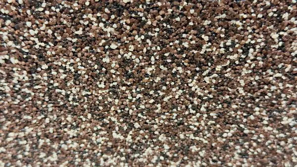 Çok renkli granüllerle dekoratif bir yüzeye yakın çekim. Kahverengi, beyaz ve siyah çakıl taşları içeren kaba doku..